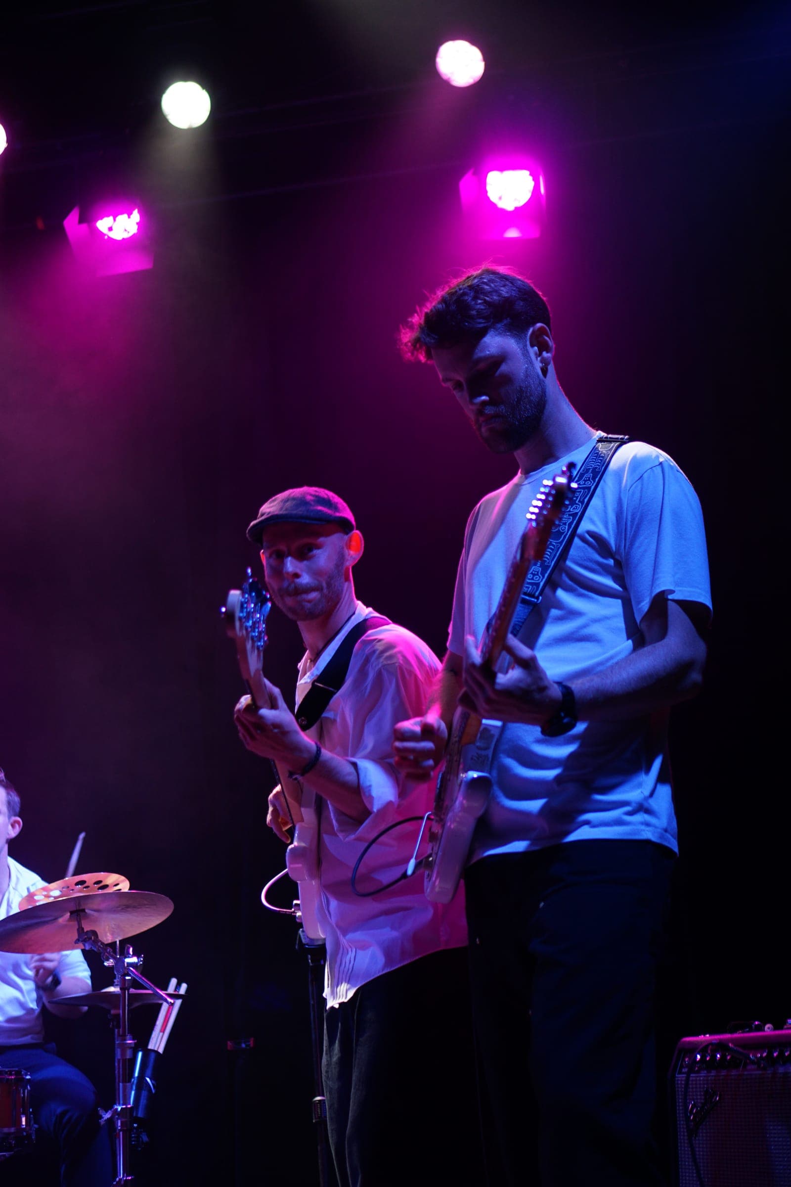 Bassist og guitarist spiller i lilla scenelys med trommeslageren ved siden af